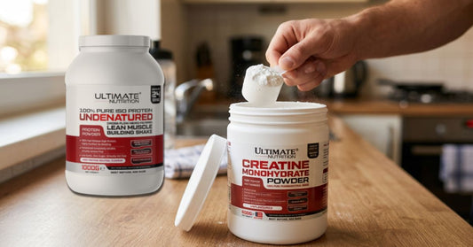 ultimate nutrition creatine monohydrate powder and pure iso protein containers on a kitchen counter with a hand scooping creatine to show how creatine and protein powder can be used together for the article can you mix creatine with protein powder