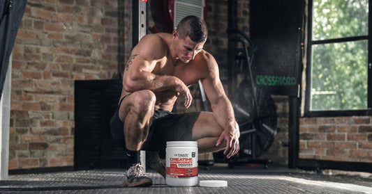 ultimate nutrition creatine monohydrate powder container in a gym setting with a muscular athlete kneeling on the floor