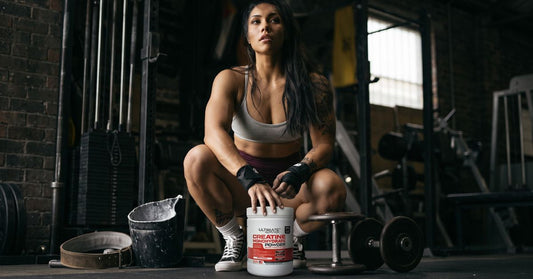 athlete in a gym crouching beside ultimate nutrition creatine monohydrate powder to illustrate how creatine supports post workout recovery during the 30 minute window for the article post workout recovery the 30 minute window explained