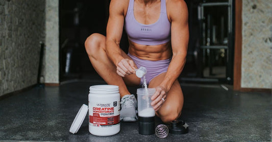athlete kneeling on gym floor scooping ultimate nutrition creatine monohydrate powder into a shaker bottle as part of a workout supplement routine for the article what is creatine and should you be taking it cavaletti collection