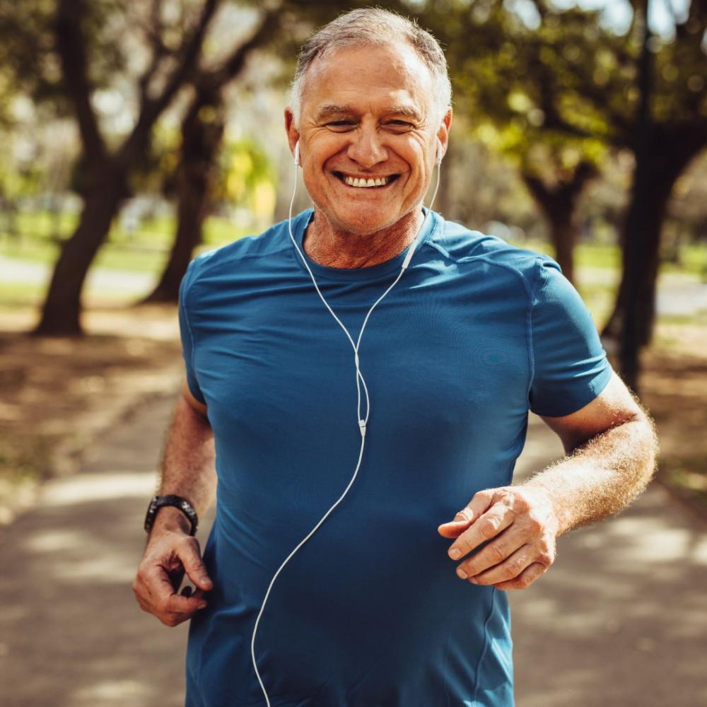 Older adult jogging on a tree-lined path wearing athletic gear and earphones, representing an active and healthy lifestyle.