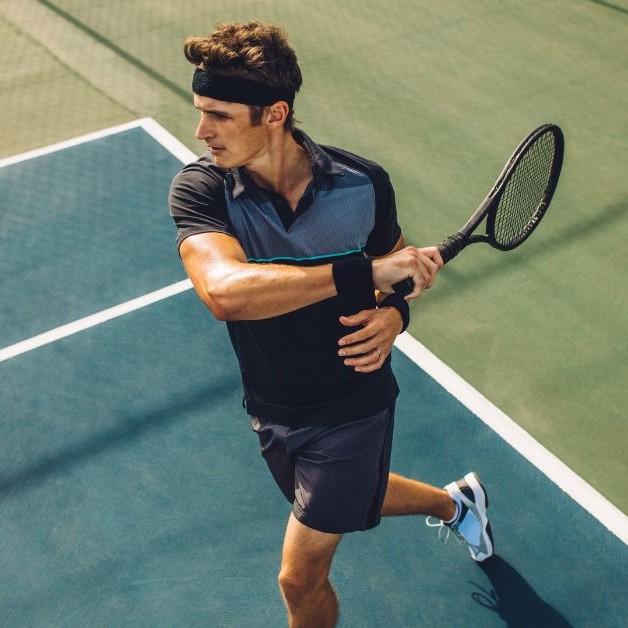 Person playing tennis on an outdoor court, captured mid-swing in athletic gear, representing strength, agility, and an active lifestyle.