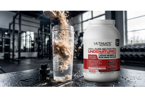 Large container of Ultimate Nutrition 100 Percent Pure ISO Protein undenatured powder on a gym surface with a scoop of protein powder being poured into a clear shaker bottle creating a dynamic splash effect with weights racks and natural light visible in 