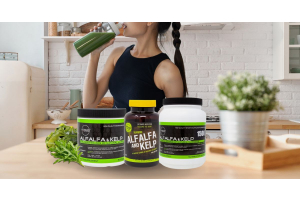 Ultimate Nutrition Alfalfa and Kelp supplement containers on a kitchen counter with fresh greens, while a person drinks a green smoothie in the background.