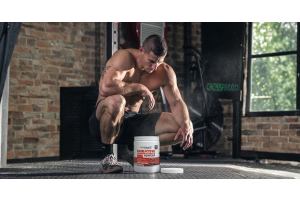 ultimate nutrition creatine monohydrate powder container in a gym setting with a muscular athlete kneeling on the floor