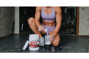 athlete kneeling on gym floor scooping ultimate nutrition creatine monohydrate powder into a shaker bottle as part of a workout supplement routine for the article what is creatine and should you be taking it cavaletti collection